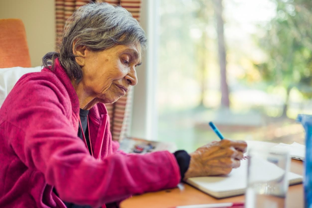 Old elderly Asian Indian woman sitting writing in a journal or notebook.